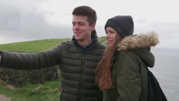 Bonita pareja toma selfies en los famosos Acantilados de Moher en Irlanda — Vídeo de stock