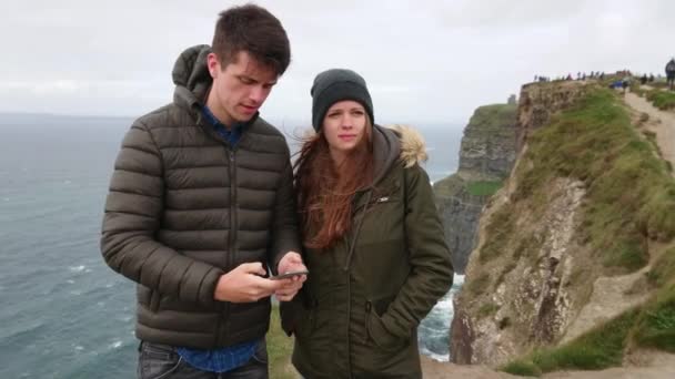 Hübsches paar macht selfies an den berühmten klippen von moher in irland — Stockvideo