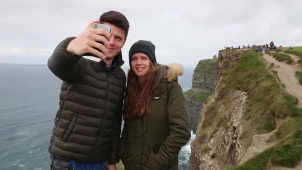 Bonita pareja toma selfies en los famosos Acantilados de Moher en Irlanda — Vídeo de stock