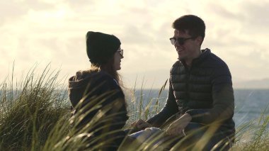 Güzel çift yüksek reed çimen kumsalda oturur.