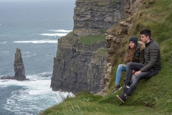 Young couple sits on the edge of the steep Cliffs of Moher in Ireland — Stock Photo, Image