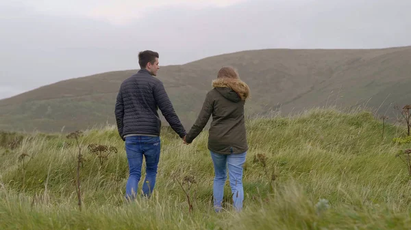 Mladý pár procházky ruku v ruce po trávnících Irska — Stock fotografie