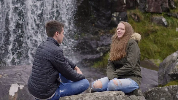 Two friends on an adventure trip to Ireland sitting in front of a waterfall