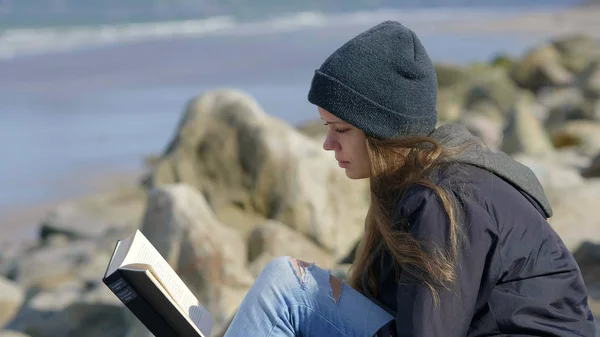Giovane donna siede al mare durante la lettura di un libro — Foto Stock