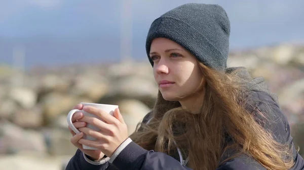 Meisje zit op de rotsen terwijl het drinken van een kopje koffie — Stockfoto