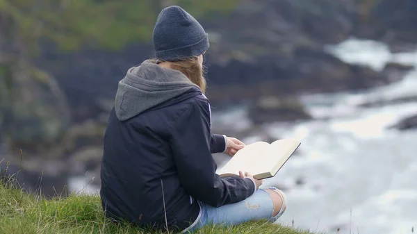 Young woman reads a book near the ocean