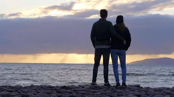 Silhueta de um casal apreciando o pôr do sol sobre o oceano — Fotografia de Stock