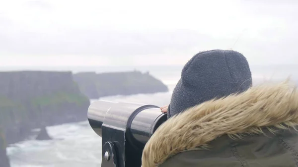 Girl looks through a spyglass over the Cliffs of Moher in Ireland — Stock Photo, Image