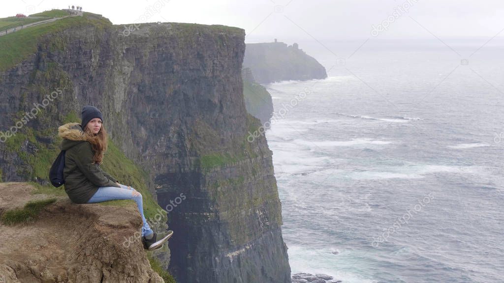 Awesome view over a girl sitting at the edge of the Cliffs of Moher