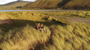 Gün batımında sahilde oturan genç bir çift üzerinde havadan görünümü