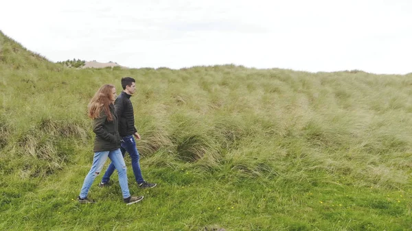 Jong koppel doorloopt een grasveld aan de Ierse kust — Stockfoto