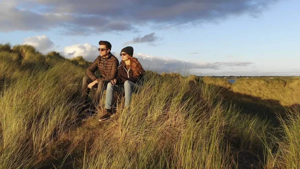 Lot od Młoda para siedzi na trawiastych wzgórzach na wybrzeżu — Zdjęcie stockowe