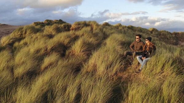 Young couple enjoy the sunset while sitting on a grassy hill