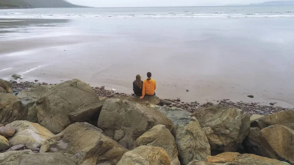 Pareja joven sentada en las rocas en la playa — Foto de Stock