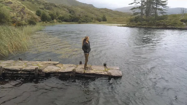 Jonge vrouw staat op een pier bij een prachtig meer in Ierland — Stockfoto