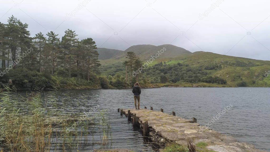 Young girl stands on a pier at a beautiful lake in Ireland