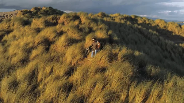 Pareja joven se sienta en una colina y disfruta de la puesta de sol — Foto de Stock