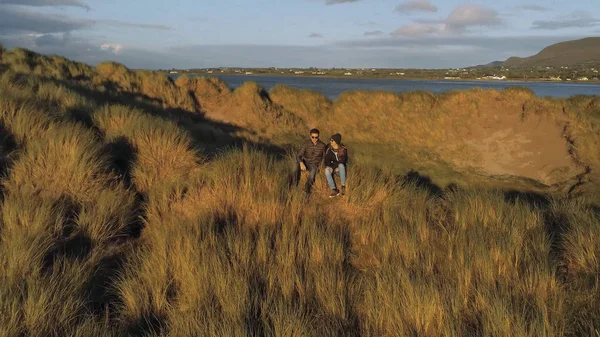 Pareja joven se sienta en la hierba y disfrutar de la puesta de sol — Foto de Stock