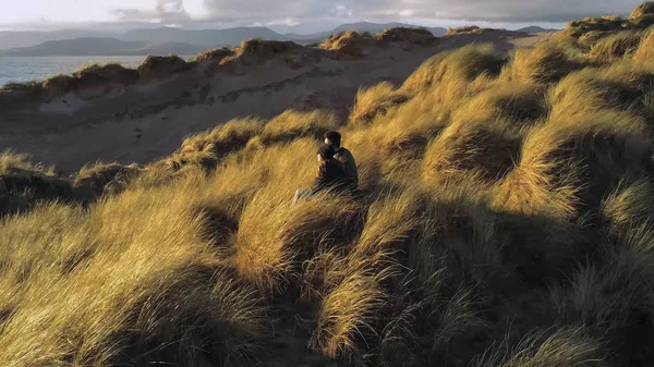 Pareja se sienta en una colina cubierta de hierba y mira hacia el atardecer — Foto de Stock