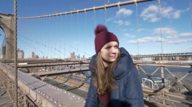 Genç güzel kadın Brooklyn Köprüsü üzerinde muhteşem manzaranın tadını çıkarırken rahatlatır