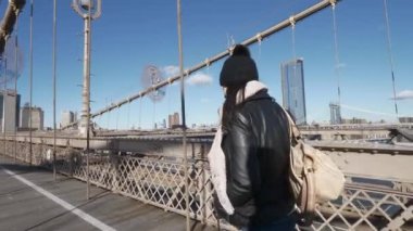 Genç kadın New York'ta Brooklyn Köprüsü üzerinde güneşli bir günde yürür.