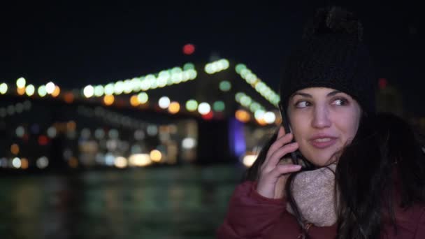 Jonge vrouw neemt een telefoontje op Brooklyn Bridge bij nacht — Stockvideo