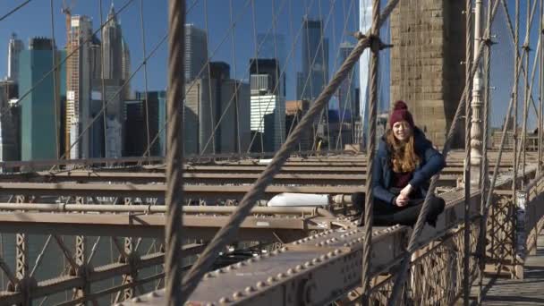 Молодая и безрассудная девушка сидит на обочине Бруклинского моста в Нью-Йорке — стоковое видео