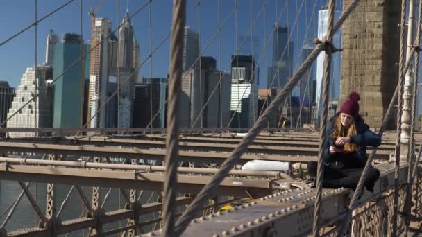 Menina bonita em Brooklyn Bridge goza de um dia ensolarado enquanto relaxa — Vídeo de Stock