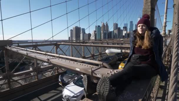 Chica joven e imprudente se sienta en el borde del puente de Brooklyn Nueva York — Vídeo de stock