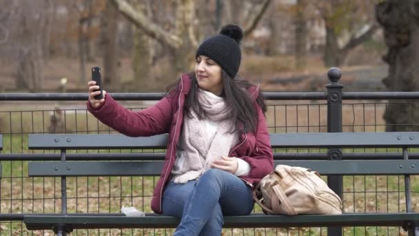 Tomarse una selfie mientras se relaja en un banco en Central Park — Vídeos de Stock