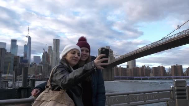 ニューヨークで二人の若い女性は、ブルックリン橋で典型的なスカイラインに沿って歩く — ストック動画