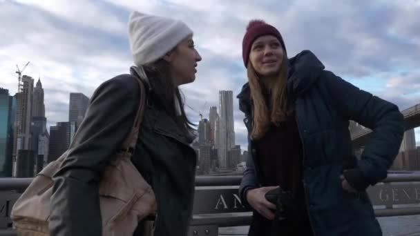 Dos mujeres jóvenes en Nueva York caminan a lo largo del horizonte típico en Brooklyn Bridge — Vídeo de stock