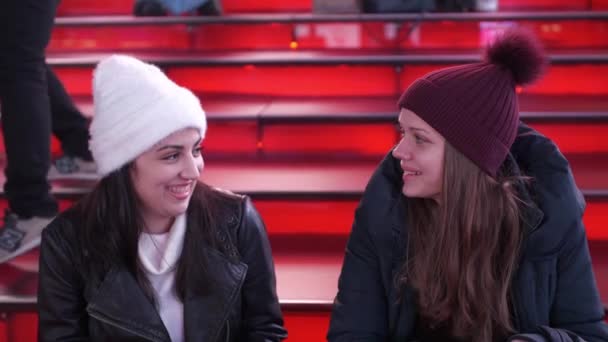 Two girls at Times Square by night sit on the famous red steps — Stock Video