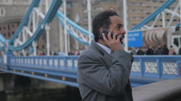 Zwarte zakenman in Londen neemt een telefoontje op Tower Bridge — Stockvideo