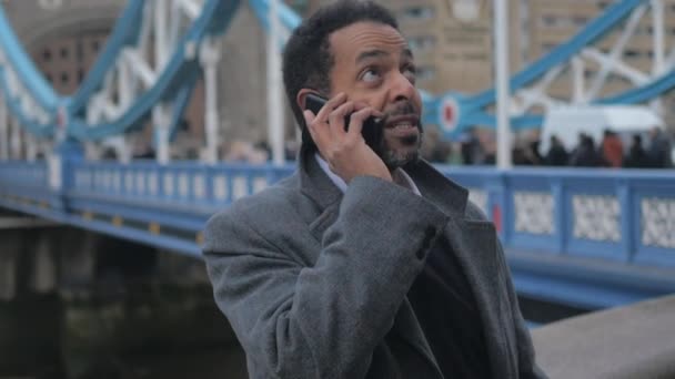 Zwarte zakenman in Londen neemt een telefoontje op Tower Bridge — Stockvideo