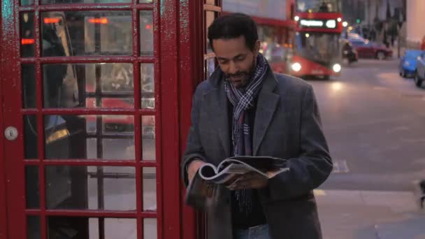 Człowiek w Londynie czyta magazyn, podczas gdy pochylony z budki telefonicznej — Wideo stockowe