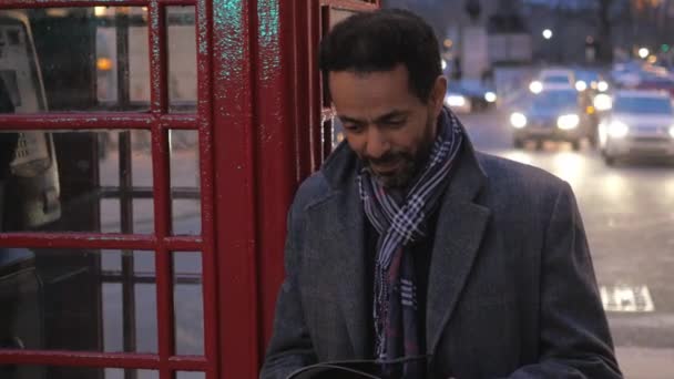 A city of London ember olvas egy magazin, miközben egy telefonfülkét támaszkodva — Stock videók