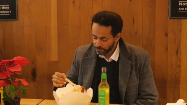 Мужчина в ресторане ест колбасу с картошкой фри — стоковое видео