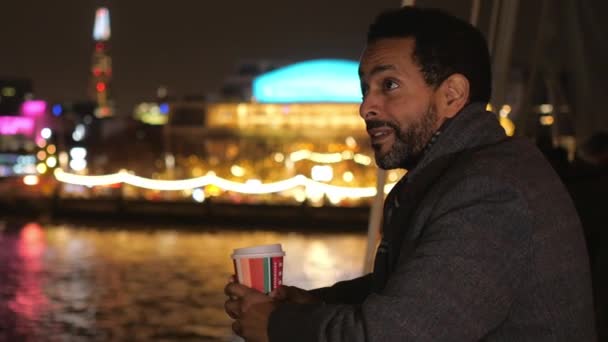 Man drinks coffee on a bridge in London and enjoys the city lights at night — Stock Video