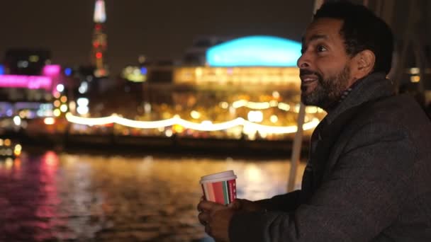 L'homme boit du café sur un pont à Londres et profite des lumières de la ville la nuit — Video