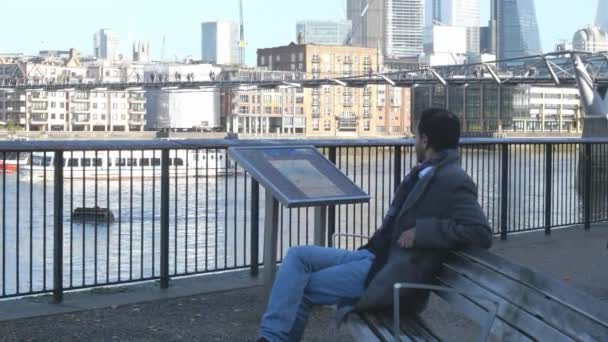 Homem de negócios negro senta-se em um banco no Rio Tâmisa Londres — Vídeo de Stock