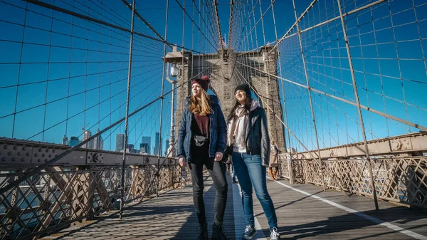 二人の女の子がニューヨークの有名なブルックリン橋を渡って歩く — ストック写真