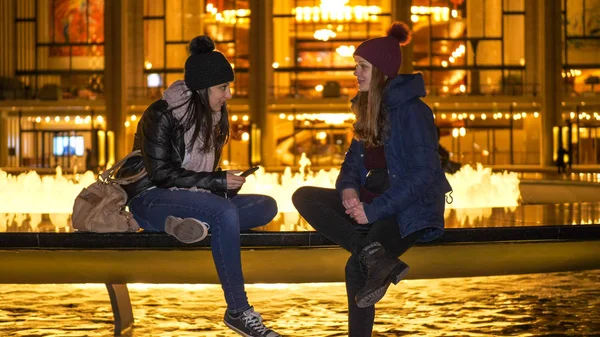 Two girls have an amazing night in New York while sitting at a fountain