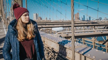 Genç güzel kadın Brooklyn Köprüsü üzerinde muhteşem manzaranın tadını çıkarırken rahatlatır