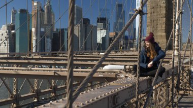 Genç ve pervasız kız Brooklyn Köprüsü'nün New York kenarında oturur