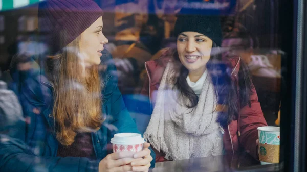 Two friends drink coffee in a cafe with a view to the street