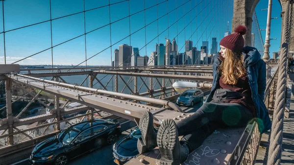 Young and reckless girl sits on the rim of Brooklyn Bridge New York — Stock Photo, Image