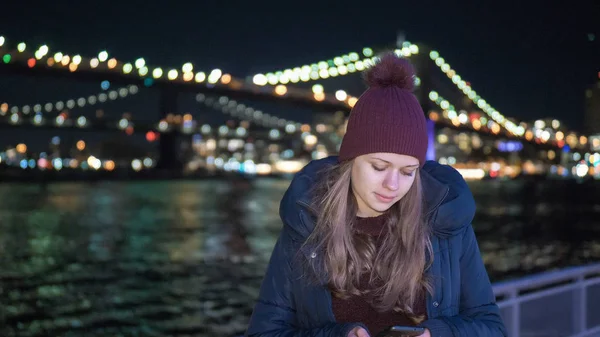 Mujer joven se sienta en Brooklyn Bridge Nueva York por la noche — Foto de Stock