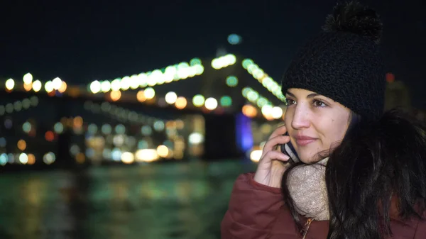 Mladá žena bere telefonní hovor na Brooklynský most v noci — Stock fotografie