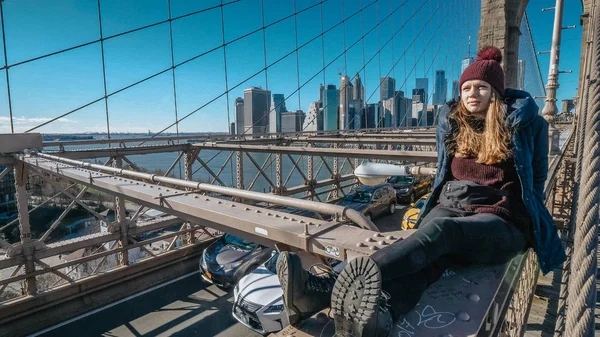 Young and reckless girl sits on the rim of Brooklyn Bridge New York — Stock Photo, Image